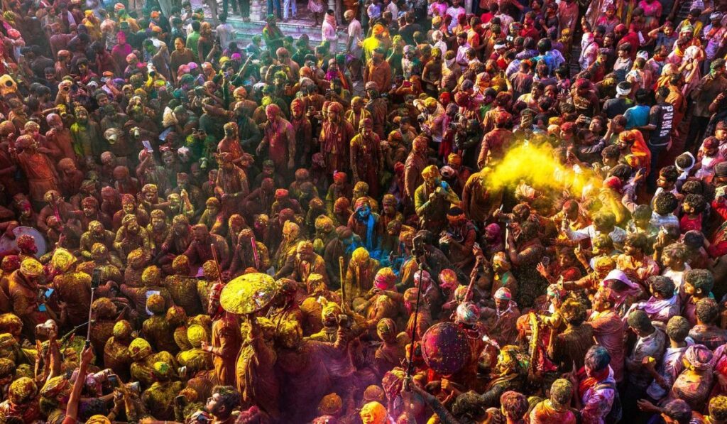 Large crowd celebrating Holi festival in Vrindavan India with colorful powder and joyful atmosphere