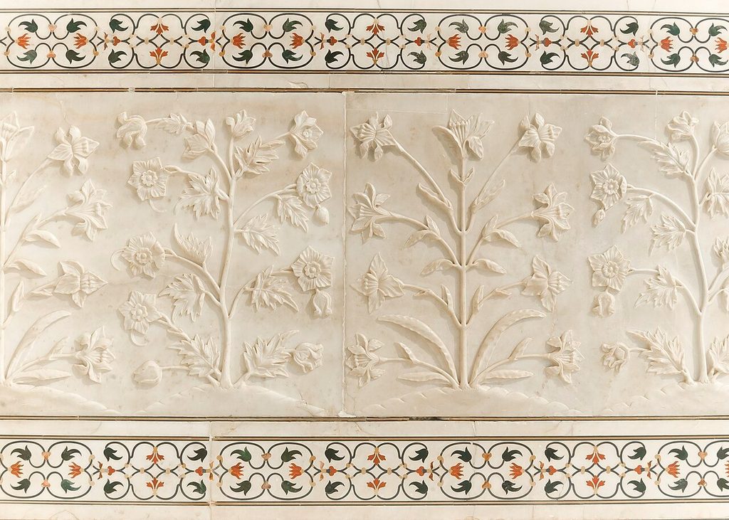 Detailed bas-relief carving of flowers and pietra dura stone inlay on white marble wall at Taj Mahal